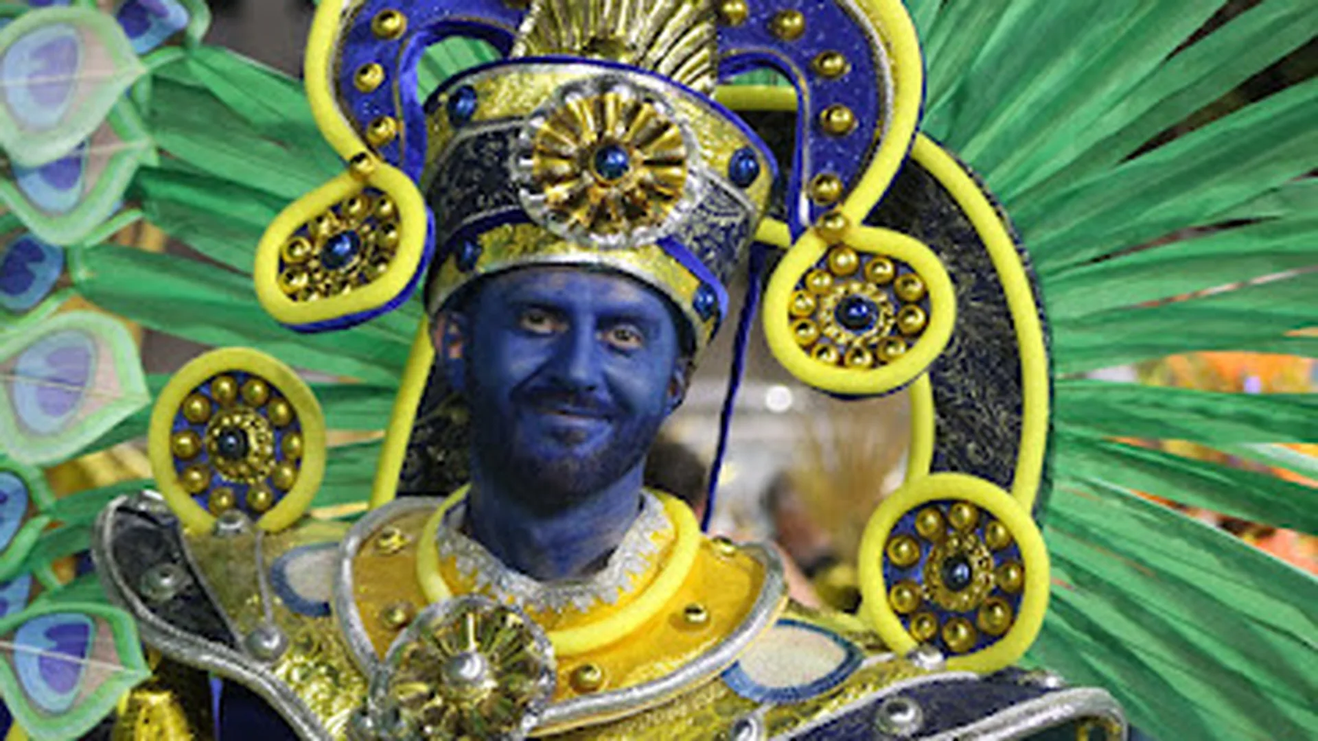 Brazilian samba dancers in colourful feathered costume performing on stage with drummers behind them
